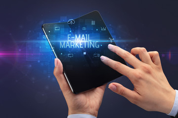 Businessman holding a foldable smartphone with E-MAIL MARKETING inscription, cyber security concept