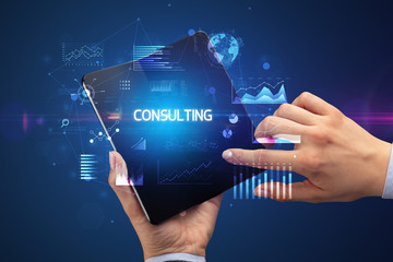 Businessman holding a foldable smartphone with CONSULTING inscription, successful business concept
