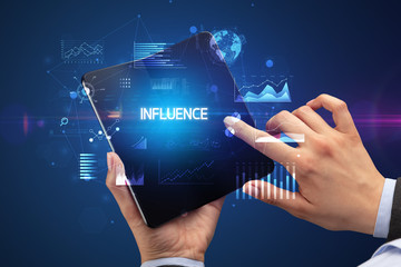 Businessman holding a foldable smartphone with INFLUENCE inscription, successful business concept