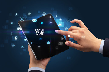 Businessman holding a foldable smartphone with SOCIAL GAME inscription, social networking concept