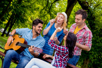 Group of friends enjoying time together in park while playing guitar