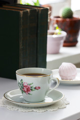 Tea in a vintage cup, marshmallows on a vintage saucer and old books on a light background.