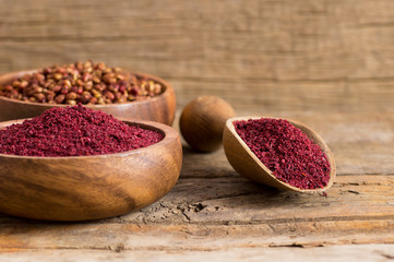 Obraz na płótnie Canvas Dried ground red Sumac powder spices in wooden spoon with sumac berries on rustic table. Healthy food concept