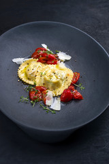 Traditionelle italienische Pasta Ravioli angeboten mit Parmesan Käse und gebratenen Tomaten als closeup auf einem Modern Design Teller