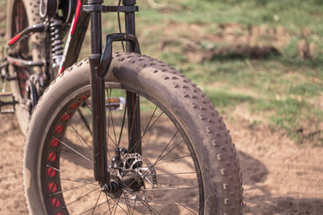 Close-up of bicycle with large wheels in countryside. Mountain bike stands on ground in sunny weather.
