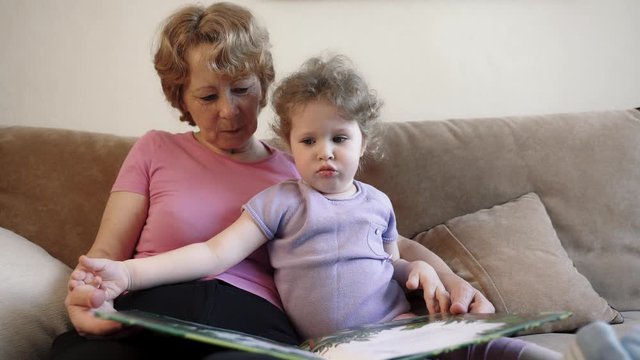 Grandmother and granddaughter together reading a book and view pictures. Happy grandmother nanny teaching grandkid learning reading at home. Grandparent and grandchild activity concept.