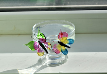 colored glass butterflies on a cup of water on a white background