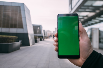 Male hand with a phone with a green screen on a background of the city