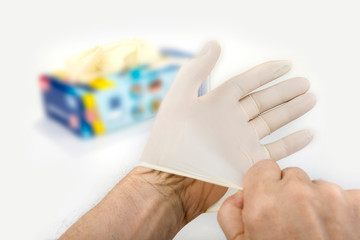 Putting rubber medical gloves on a hand o n a white