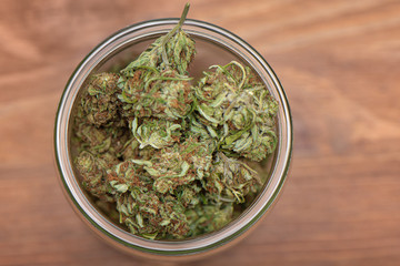 Top down shot of glass full of green dried cannabis buds  on wooden table. 