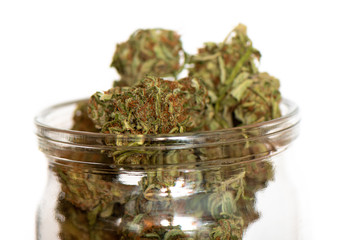 Fototapeta na wymiar Shot of glass jar full of green dried cannabis buds on wooden table. 