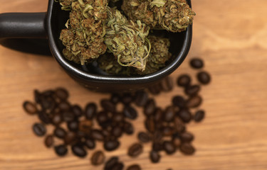 Top shot of black coffee cup full of dried green cannabis buds and some coffee beans on wooden table