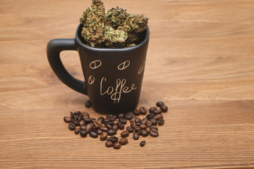 Black coffee cup full of dried green cannabis buds and some coffee beans on wooden table