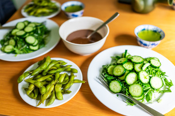 Wooden table and green salad dish with Japanese cucumbers and mizuna greens and boiled edamame soy beans with tea at home lunch dinner