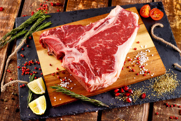 Raw T-bone Steak for grill or BBQ on cutting board over aged wooden background