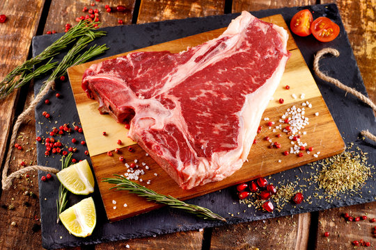 Raw T-bone Steak For Grill Or BBQ On Cutting Board Over Aged Wooden Background