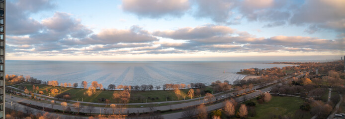 Highrise condo buildings along Sheridan Road near Lake Shore Drive cast long shadows along the lakefront and Lake Michigan as white fluffy clouds float in the sky above.