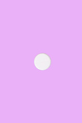 Round medical pill with a dividing notch on a pink background.