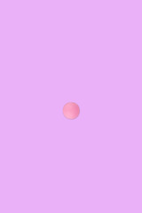 Round pink medical pill on a pink background.