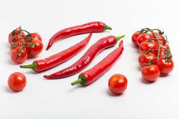 Juicy red hot chili peppers with cherry tomatoes on a branch on a white background