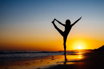 Fototapeta na wymiar Girl at sunset, on the ocean shore doing yoga