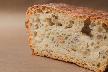 Homemade rye-wheat yeast-free bread with live sourdough. A loaf of rye-wheat bread with flax and sunflower seeds in a close-up section on a beige linen fabric
