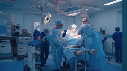 Team of surgeons doing plastic surgery in modern clinic. Group of medical workers in blue uniform perform an operation to a patient. - Powered by Adobe