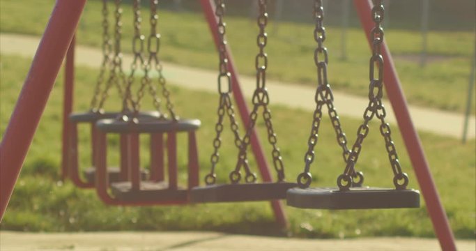 Empty chain swingset sways earily in abandoned park, telephoto