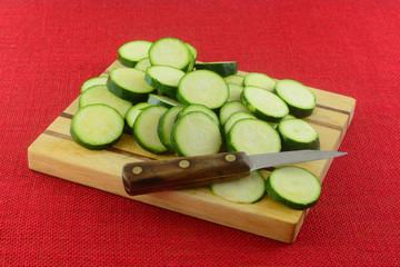 Sliced fresh raw zucchini squash on wooden cutting board with knife