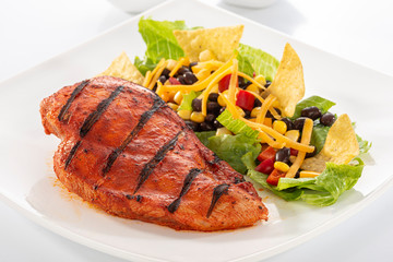 Mexican style marinated grilled chicken breast with fresh salads and green herb pesto on white rectangle plate