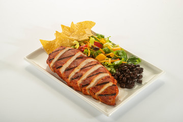 Mexican style marinated grilled chicken breast with fresh salads and green herb pesto on white rectangle plate