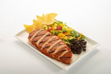 Mexican style marinated grilled chicken breast with fresh salads and green herb pesto on white rectangle plate