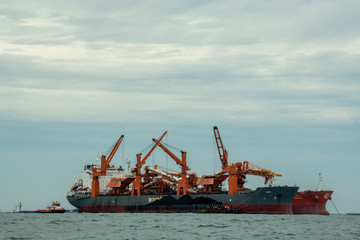 Loading coal from cargo barges onto a bulk vessel using ship cranes  in offshore coal cargo terminal.
