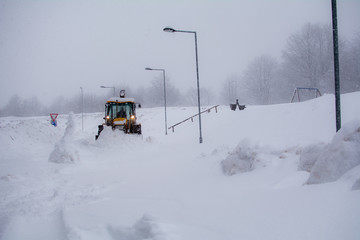 Yellow excavator clears the snow in the ski resort. Snowy days, road covered with snow. Winter landscape on mountain