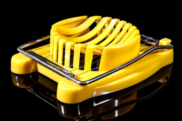 View of manual yellow plastic boiled egg cutter with steel wires on the frame isolated on black...