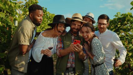 Positive farmer using smartphone calling his friends watching fun videos on mobile screen staying in grapevine valley outdoor.