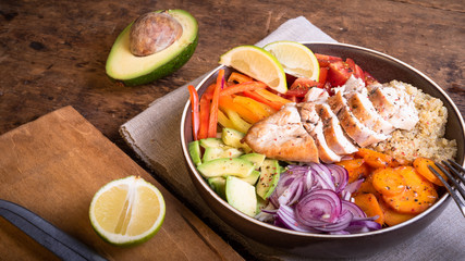 American delicious salad with chicken breast, vegetables, avacado, lettuce and quinoa in a plate on a wooden table