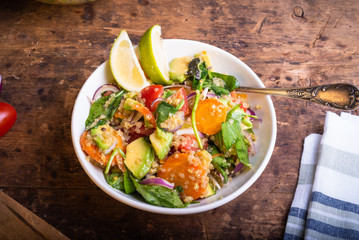 American vegetarian salad with vegetables, avacado, lettuce and quinoa in a plate with lime slices on a wooden table