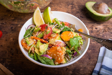 American vegetarian salad with vegetables, avacado, lettuce and quinoa in a plate with lime slices on a wooden table