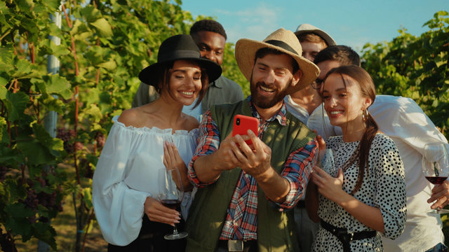 Positive farmer using smartphone calling his friends watching fun videos on mobile screen staying in grapevine valley outdoor.