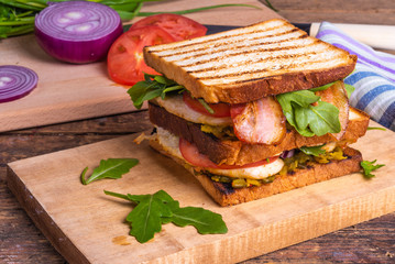 Large delicious homemade square sandwich with chicken breast, bacon, salad and vegetables