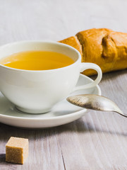 Cup of tea with croissant and a slice of sugar on a wooden table close-up
