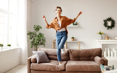 Cheerful woman listening to music and dancing on soft couch at home in day off.