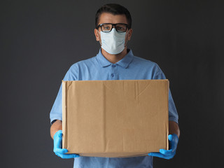 Man in medical mask and gloves delivered the parcel. Courier with a cardboard box. Parcel Delivery Service during Epidemic pandemic coronavirus 2019-ncov, covid-19 virus.