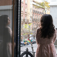 Beautiful latina girl on a balcony in the streets of Madrid thinking with colorful buildings in the background