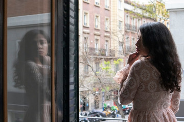 Beautiful latina girl on a balcony in the streets of Madrid thinking with colorful buildings in the background