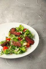 salad with beef steak cherry tomatoes and cheese in white plate on concrete table background