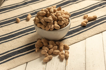 inshell peanuts in a white ceramic bowl on a cloth tablecloth and white wooden table