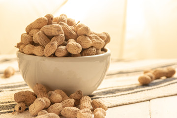 inshell peanuts in a white ceramic bowl on a cloth tablecloth and white wooden table