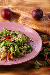 plum salad with herm microgreen and pine nuts in plate on wooden table.